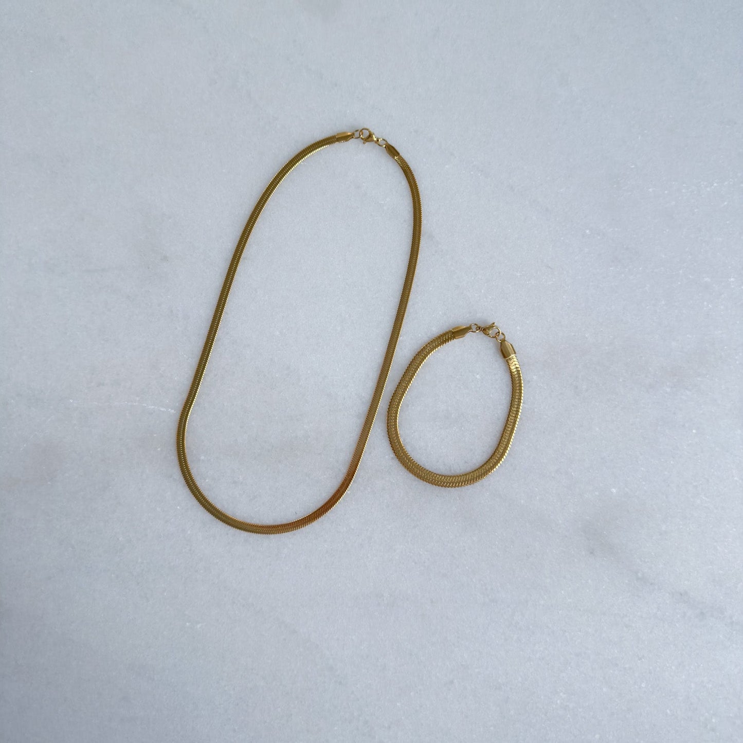 Gold herringbone necklace and bracelet set on a light gray background