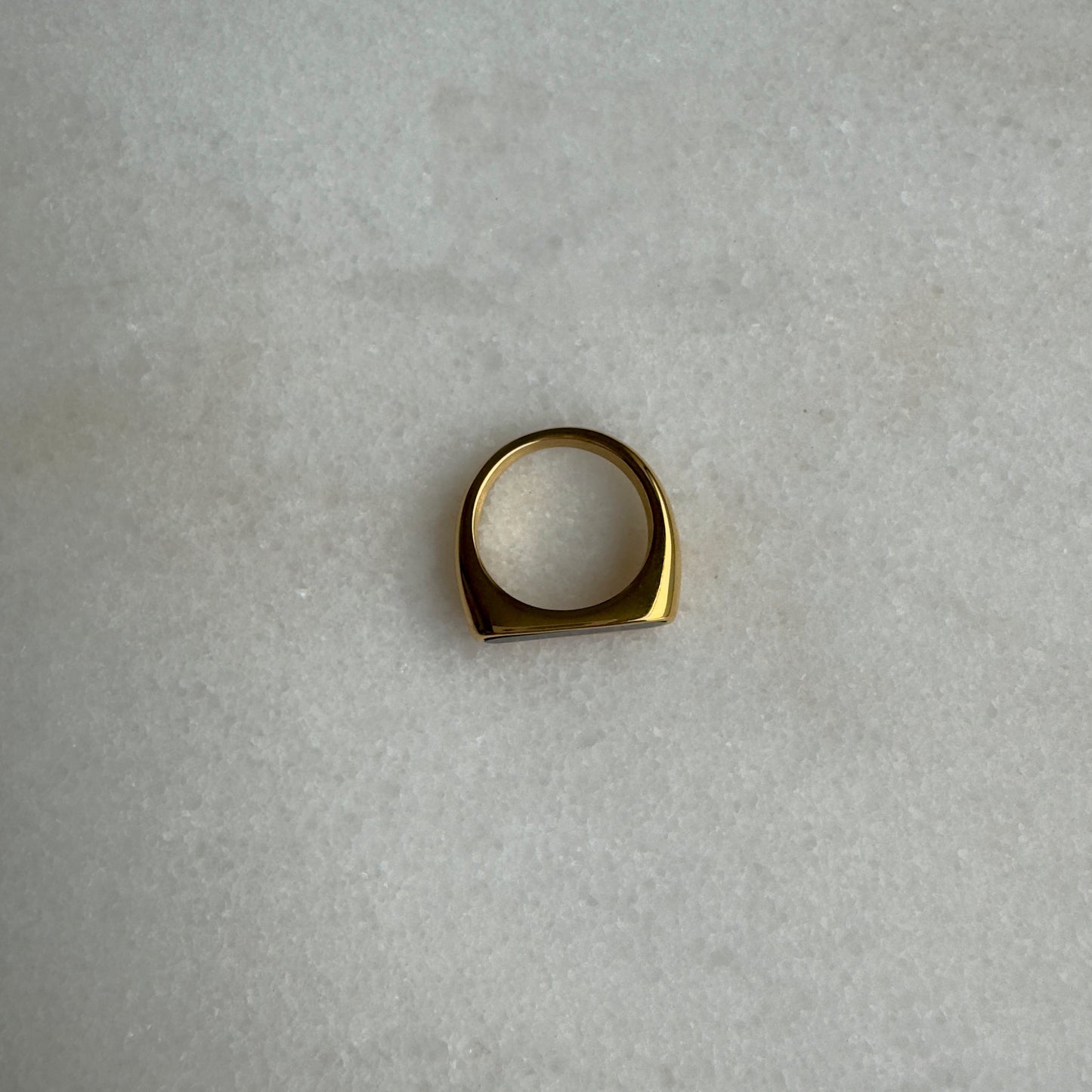 Gold signet ring with black enamel on marble background