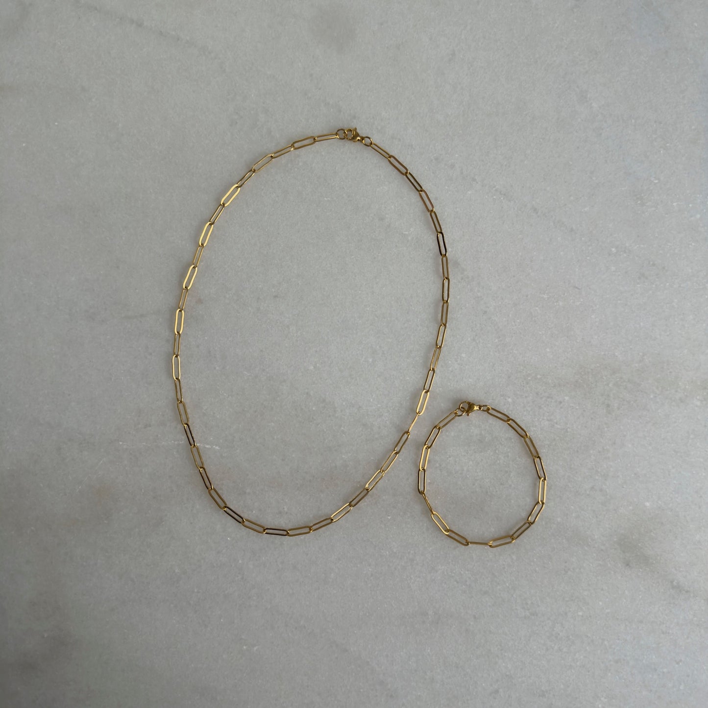 Gold Paperclip Bracelet with matching necklace on marble background