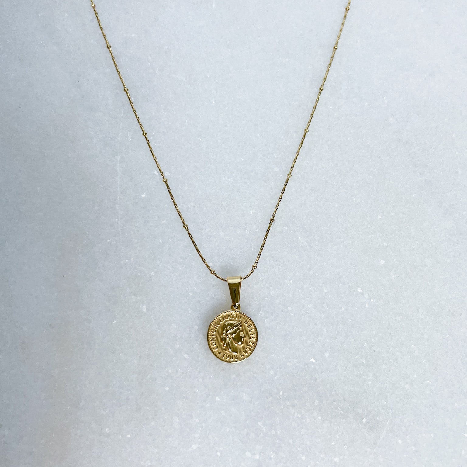 Gold necklace with a round pendant on a white background