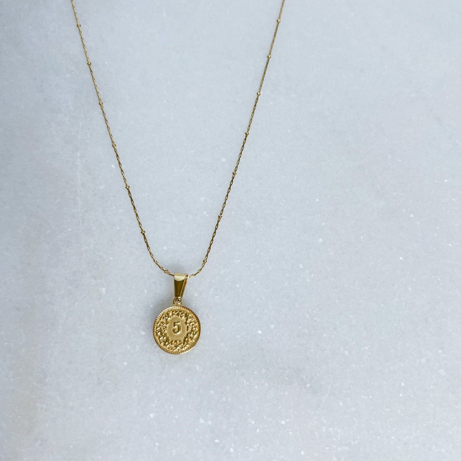 Gold necklace with a round pendant on a light gray background