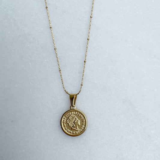 Gold necklace with a round pendant on a light gray background