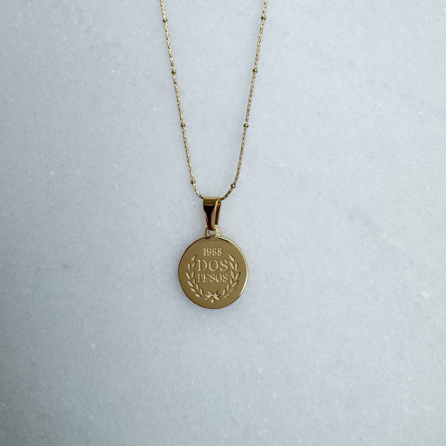 Gold necklace with a round pendant on a light gray background