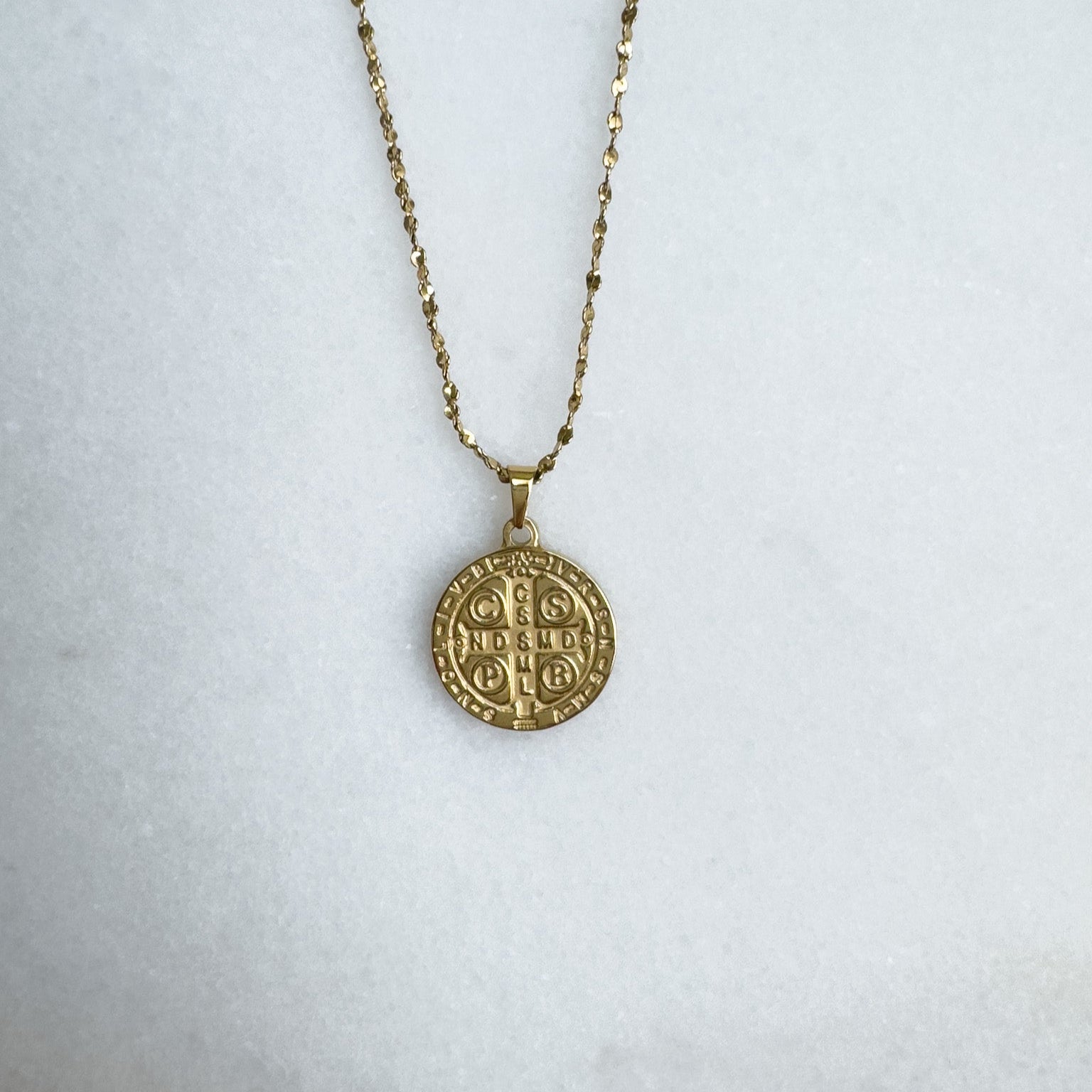 Gold necklace with a large round pendant on a light gray background