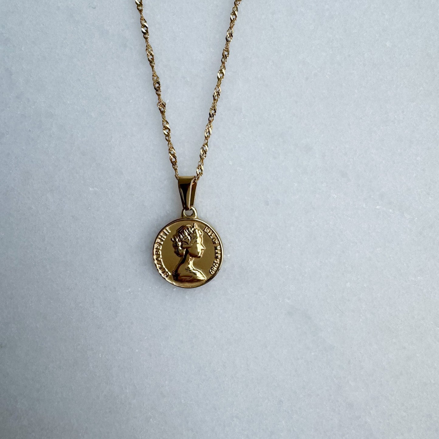Gold necklace with a round pendant on a light gray background
