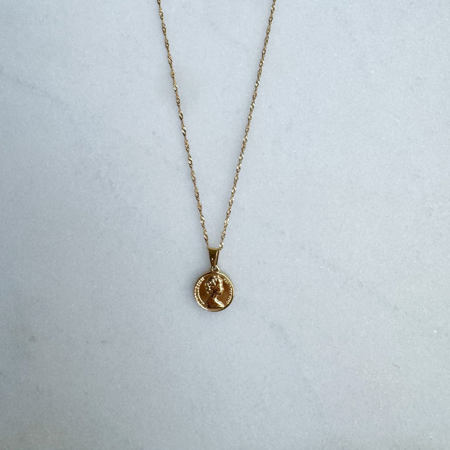 Gold necklace with a coin pendant on a white surface