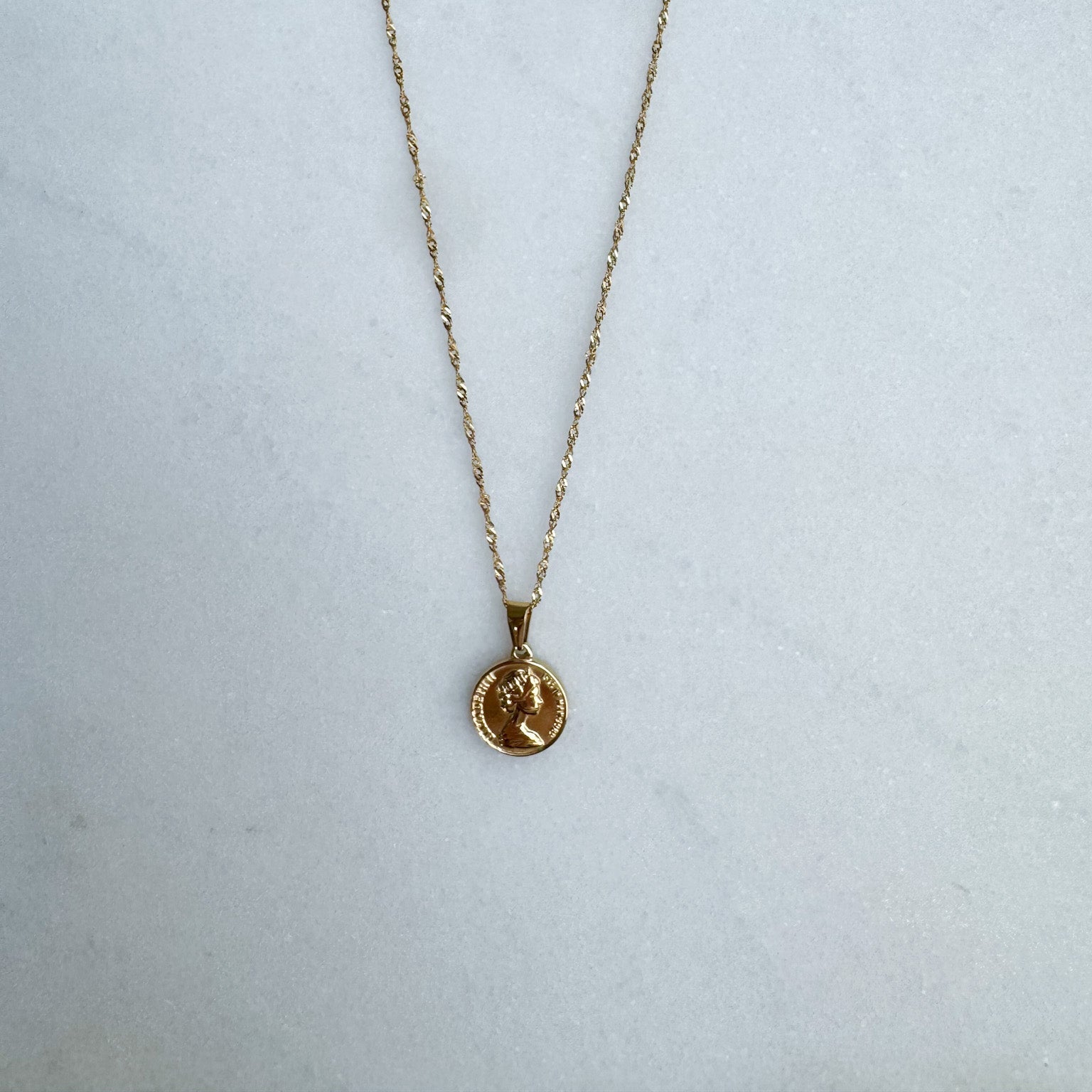 Gold necklace with a coin pendant on a white surface