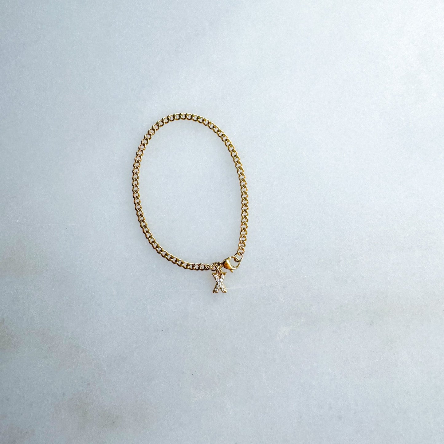 Gold chain bracelet with a small initial charm on a light gray background