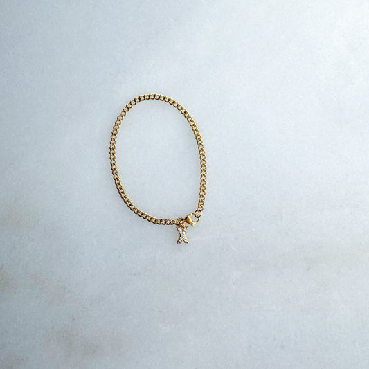 Gold chain bracelet with a small initial charm on a light gray background