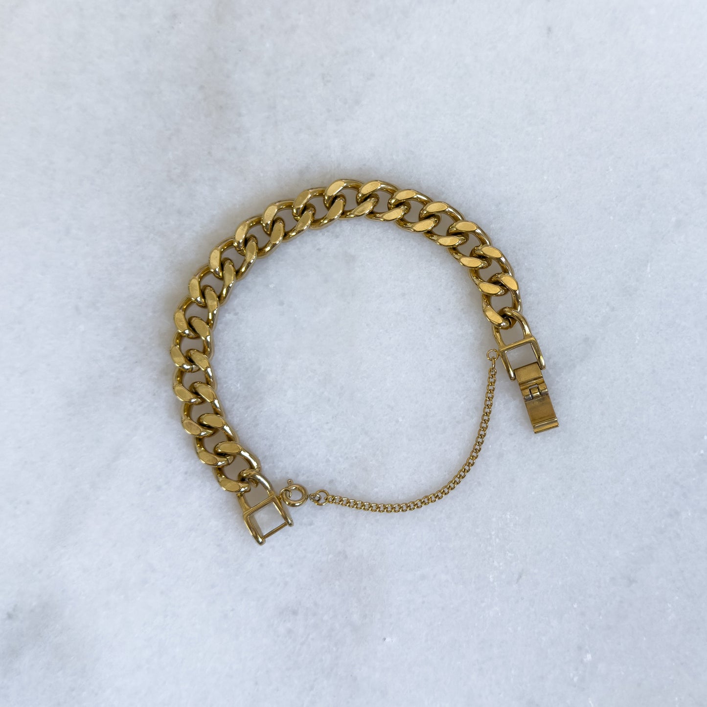 18K gold-plated 10mm cuban link bracelet with safety chain opened on marble background