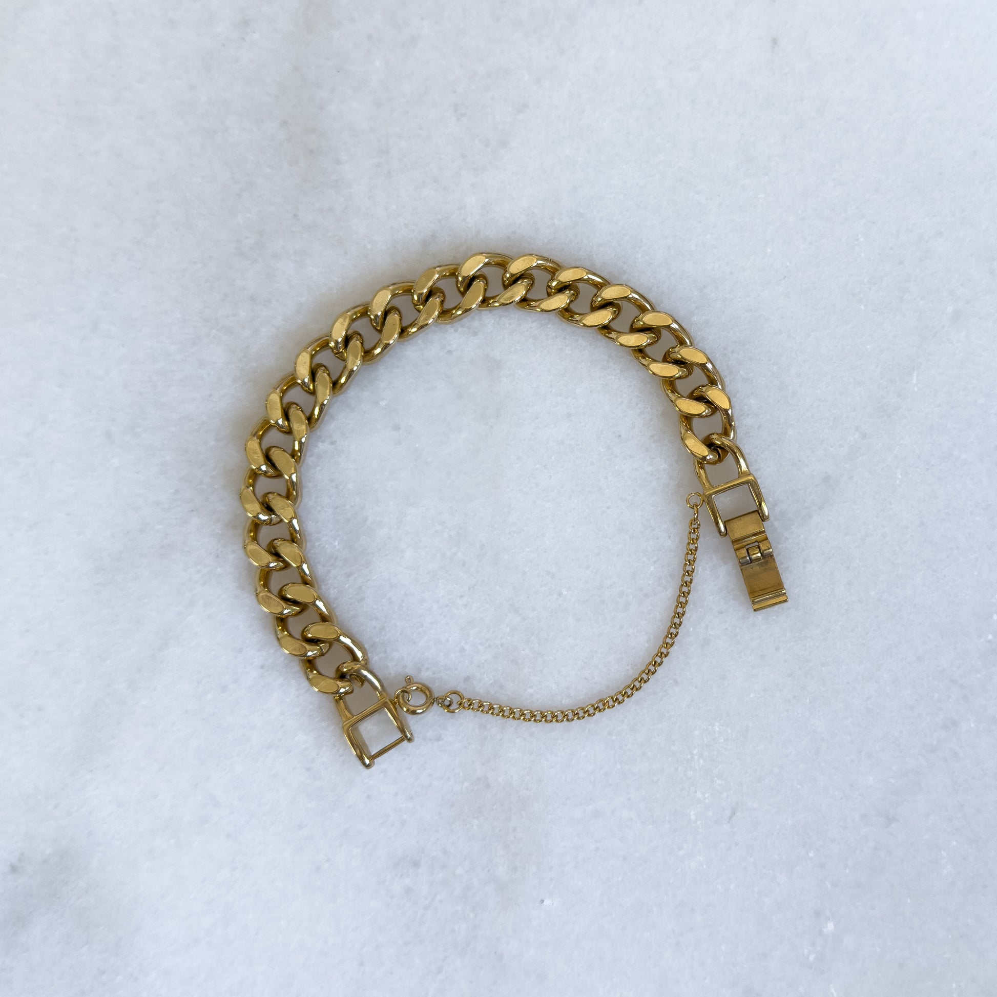 18K gold-plated 10mm cuban link bracelet with safety chain opened on marble background