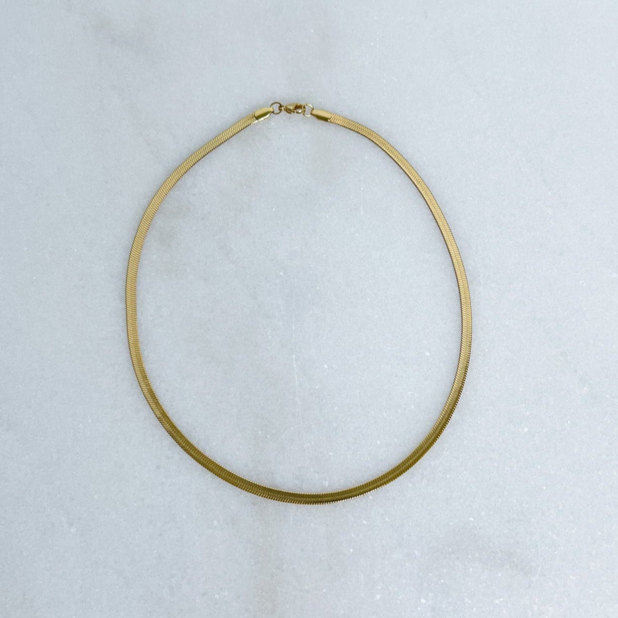 Gold herringbone necklace on a white marble surface