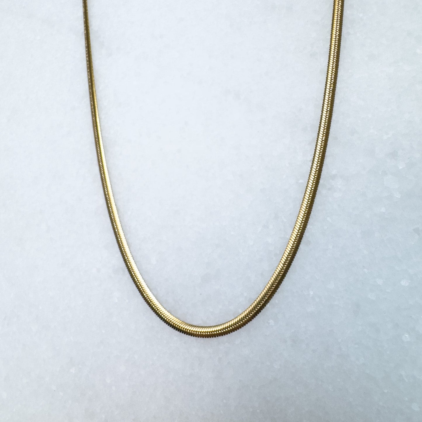 Gold herringbone chain necklace on a light gray background