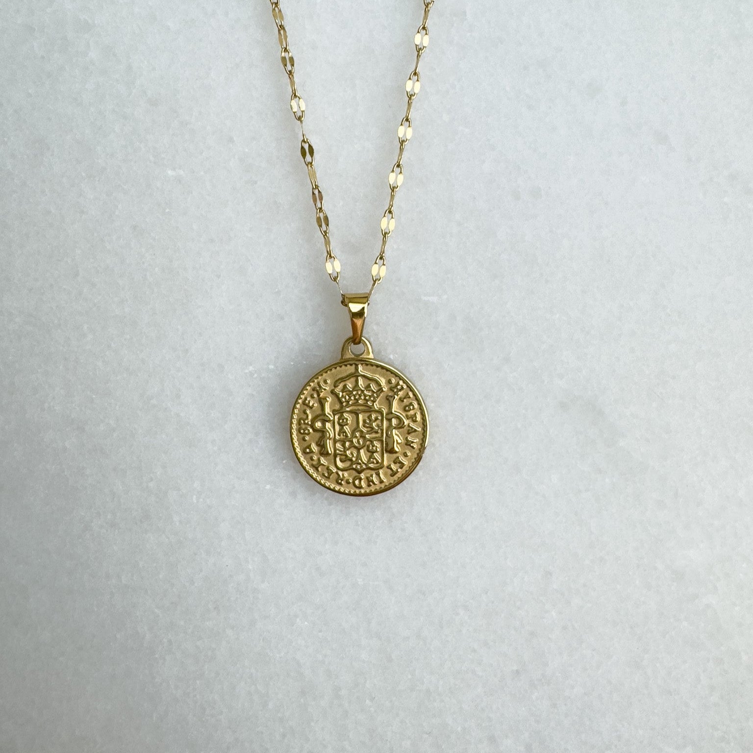 Gold necklace with a coin pendant on a light gray background