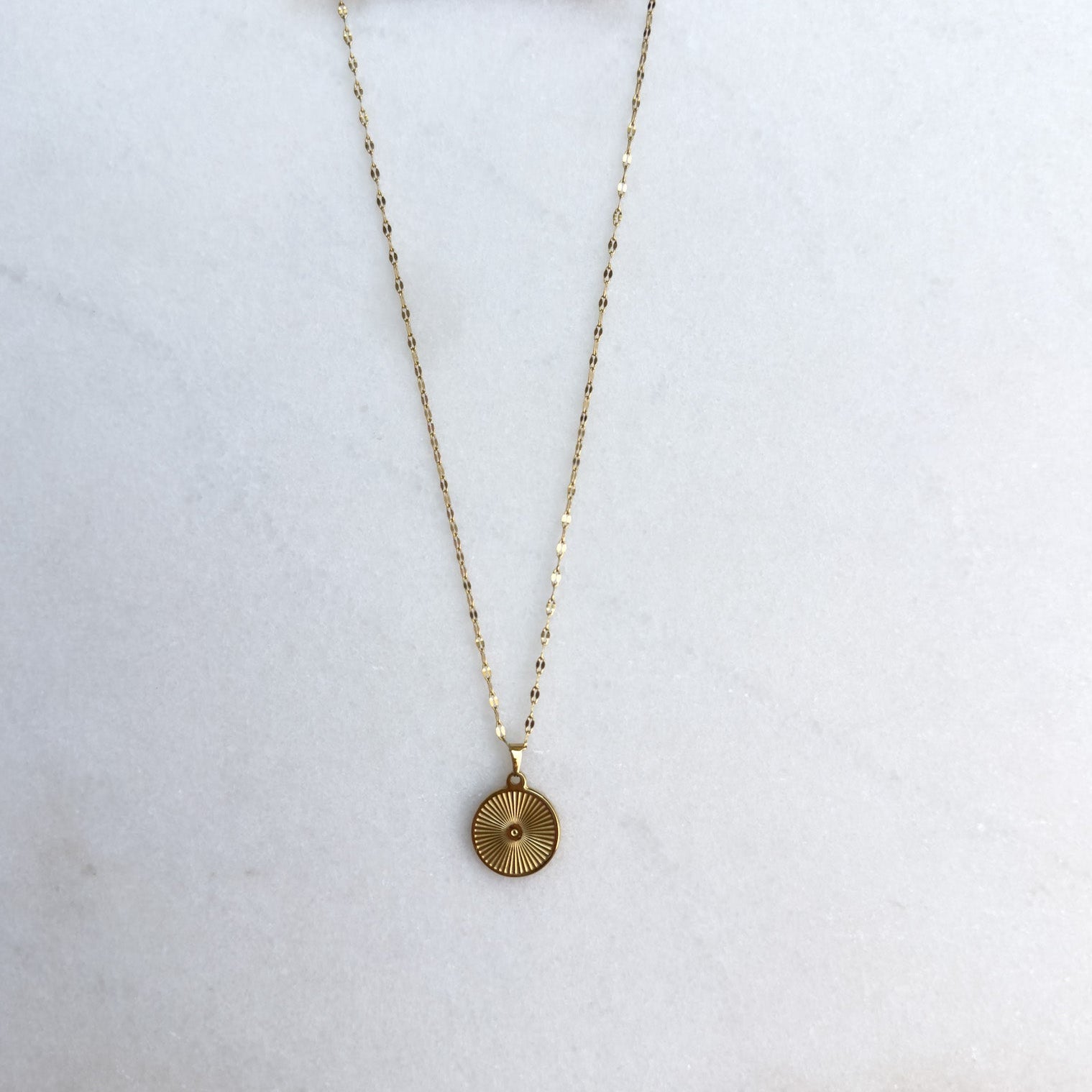 Gold necklace with a round pendant on a white surface