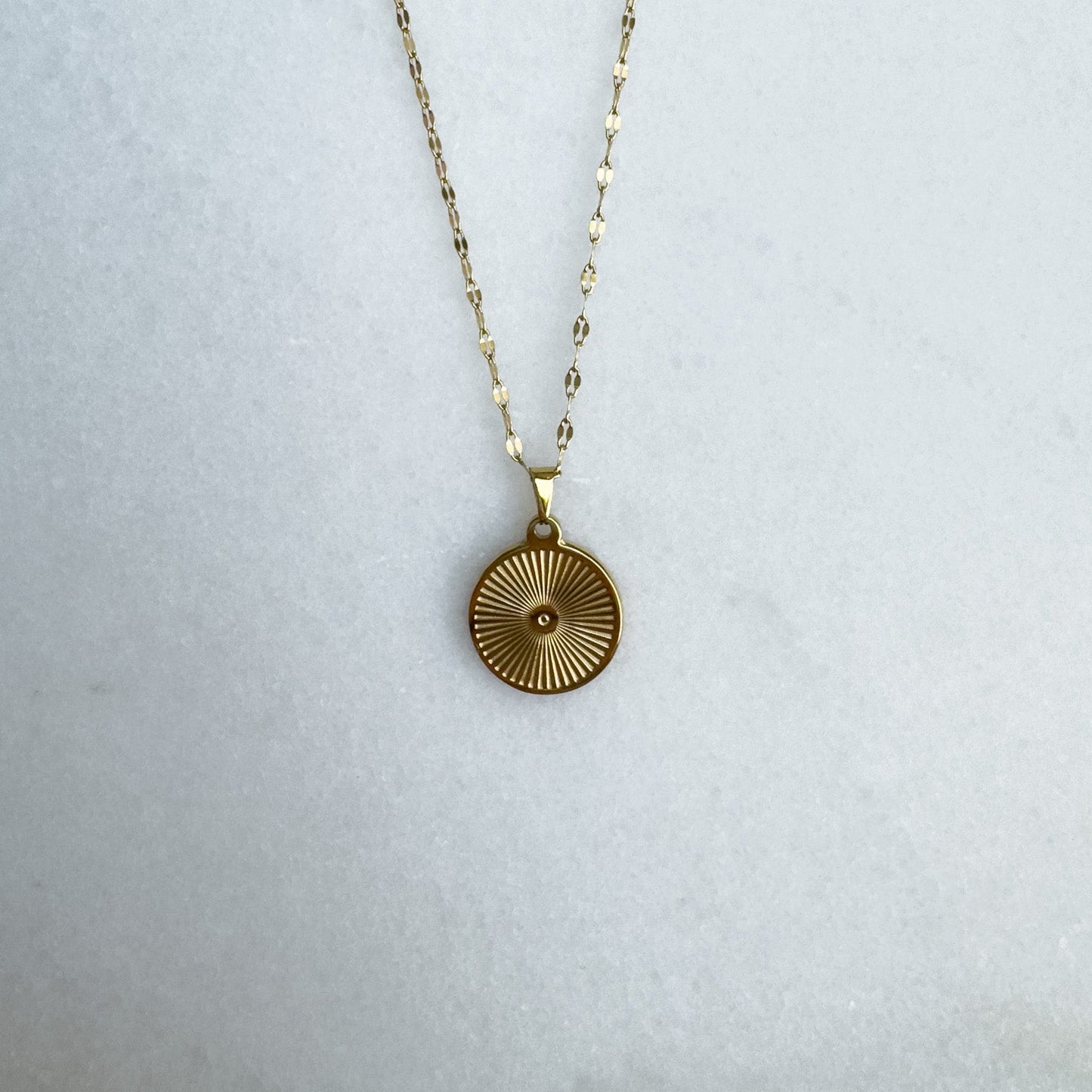 Gold necklace with a circular pendant on a light gray background
