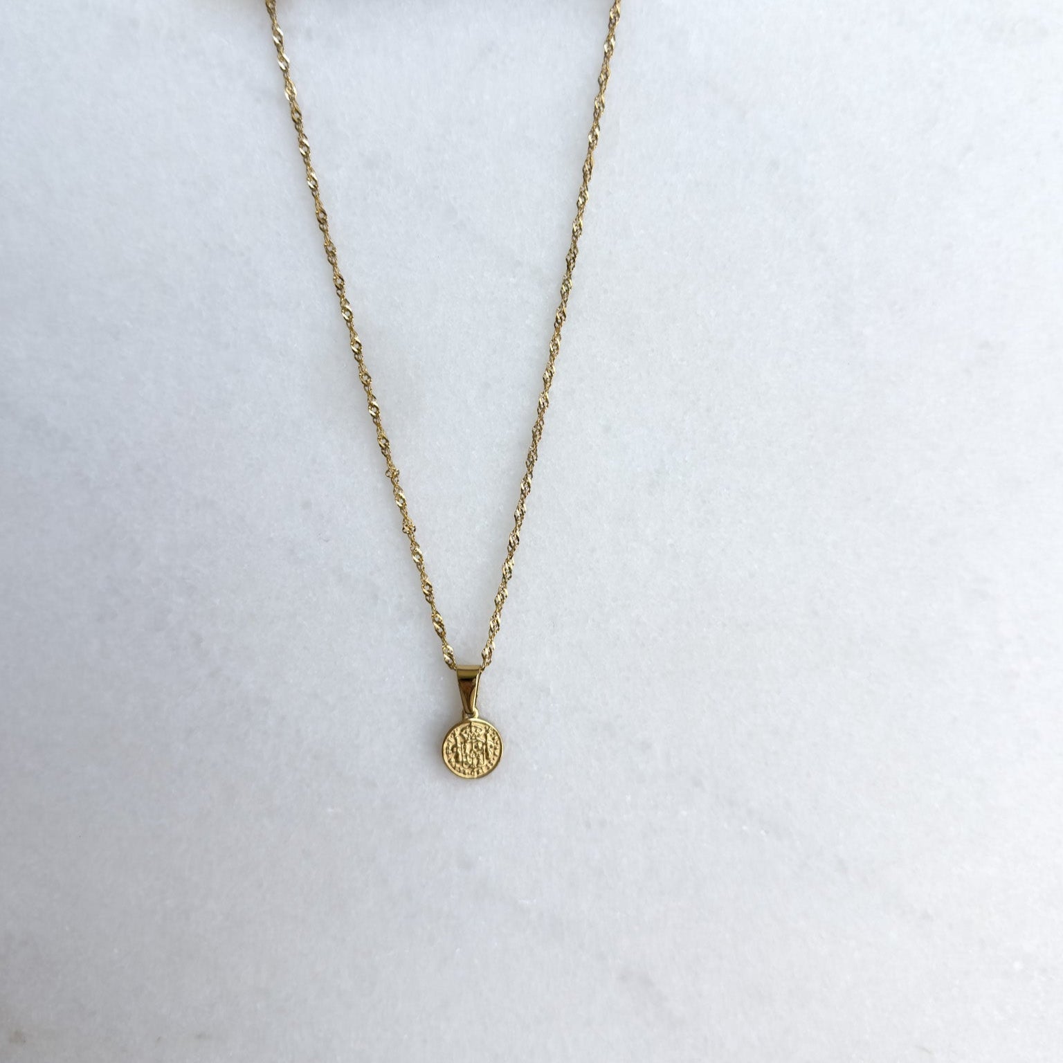 Gold necklace with a pendant on a white surface