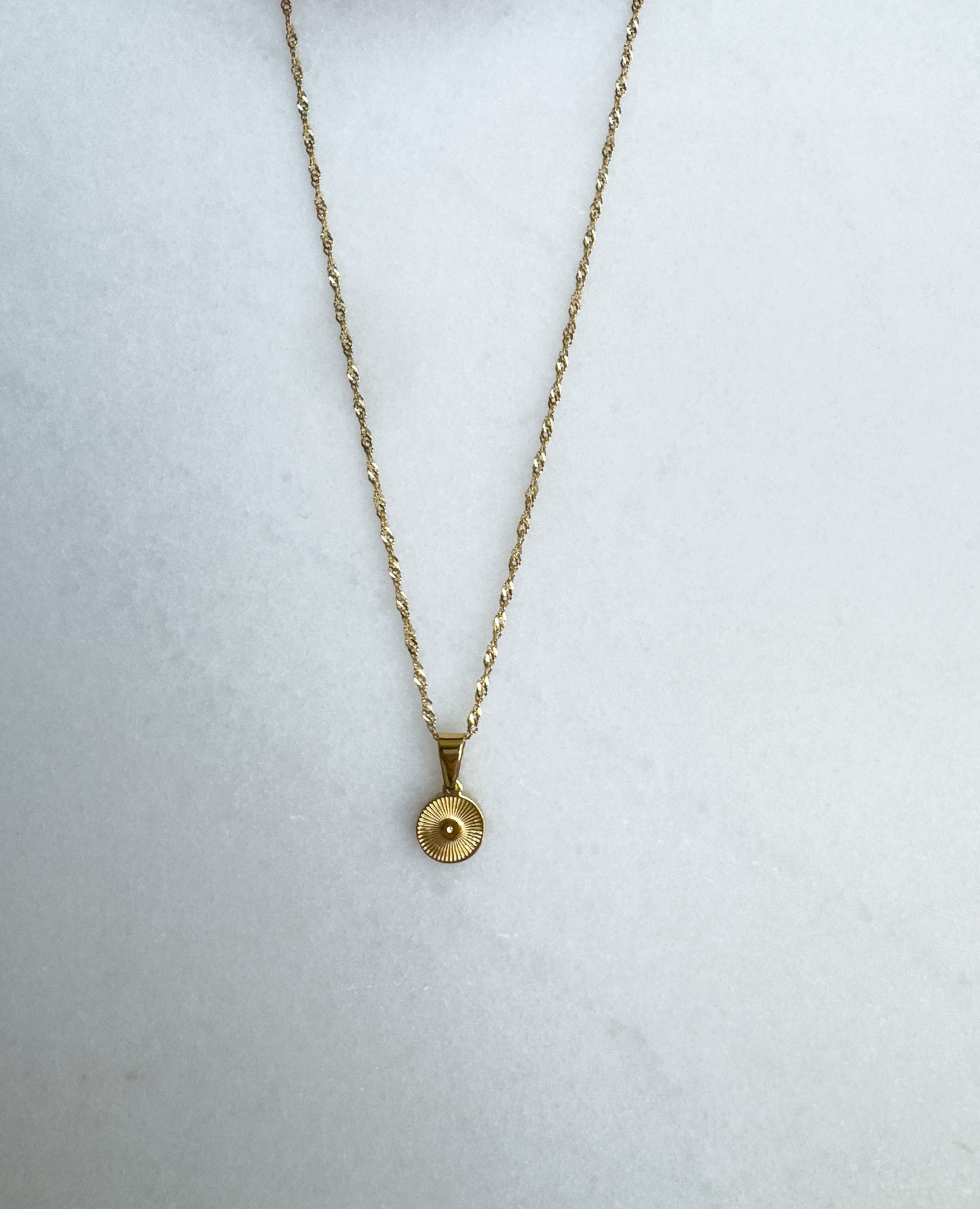 Gold necklace with a round pendant on a white background