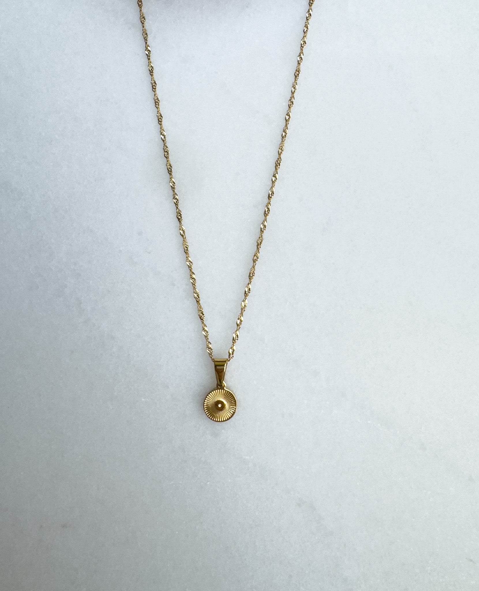 Gold necklace with a round pendant on a white background