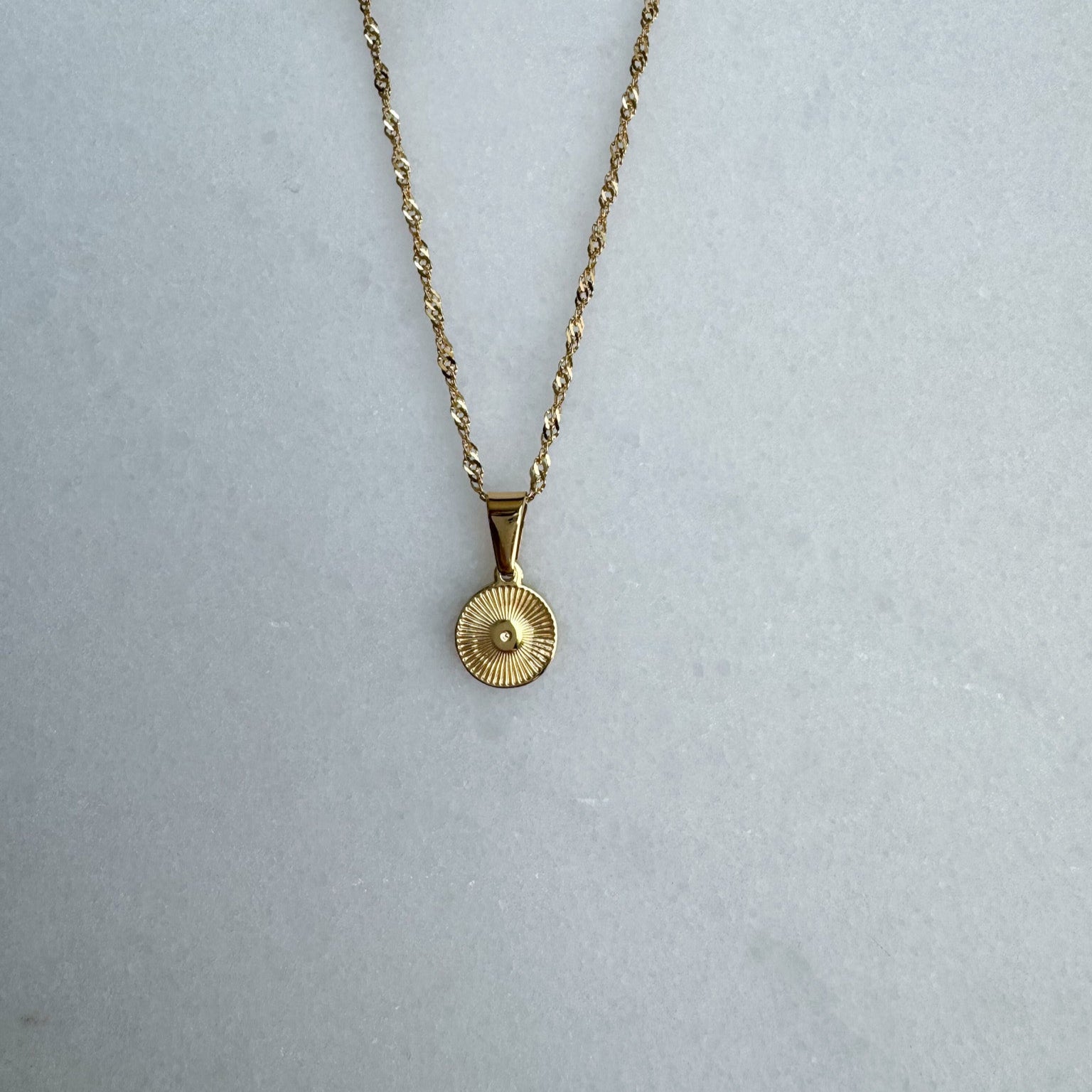 Gold necklace with a round pendant on a light gray background