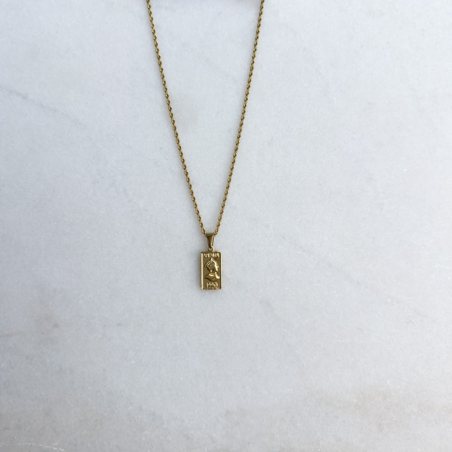Gold necklace with a rectangle pendant on a white surface