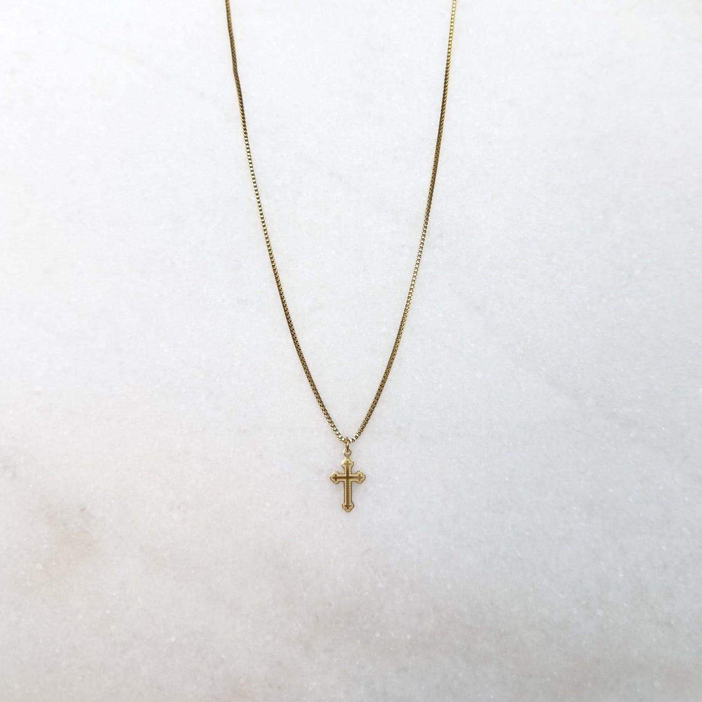 Gold necklace with a cross pendant on a white surface 