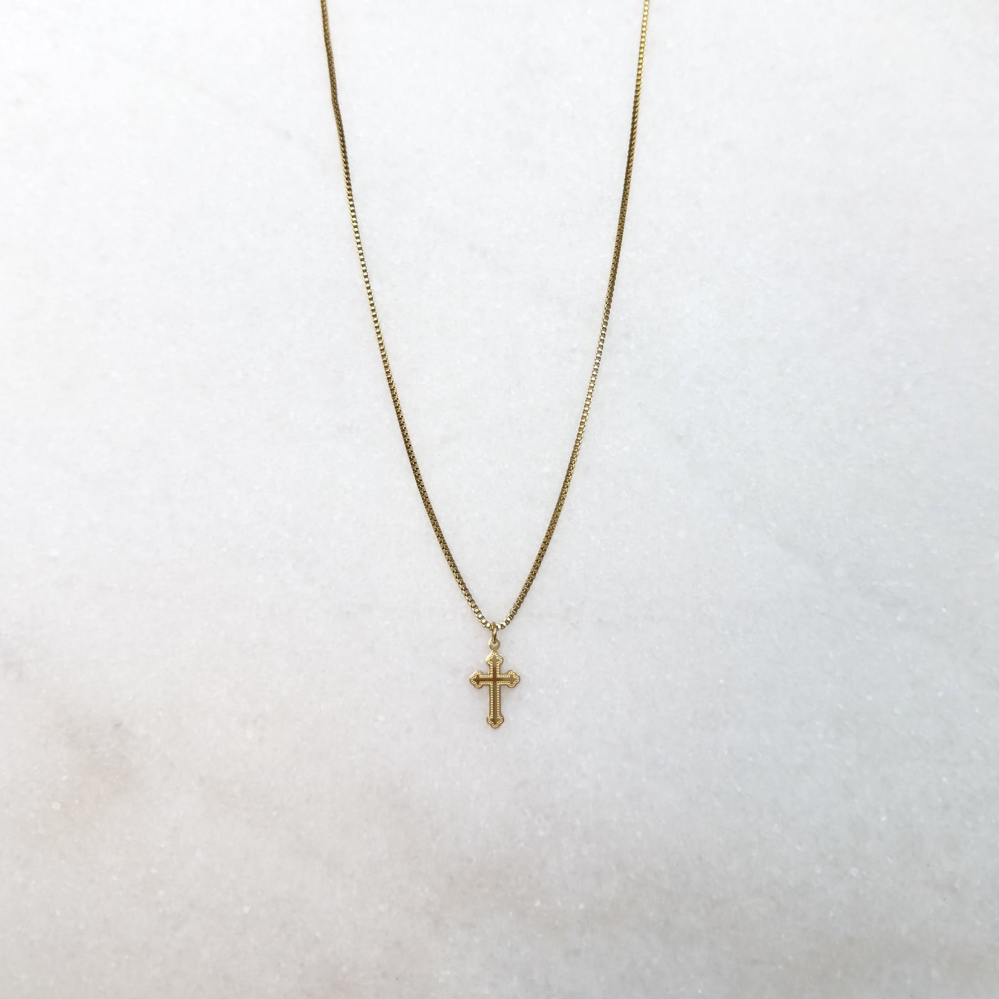 Gold necklace with a cross pendant on a white surface 
