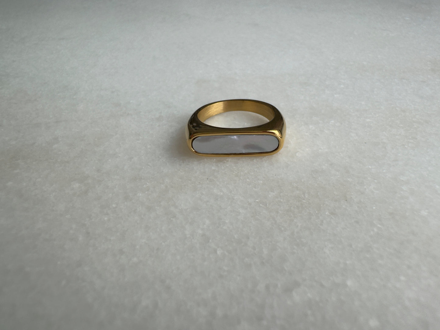 Gold signet ring with white enamel on marble background