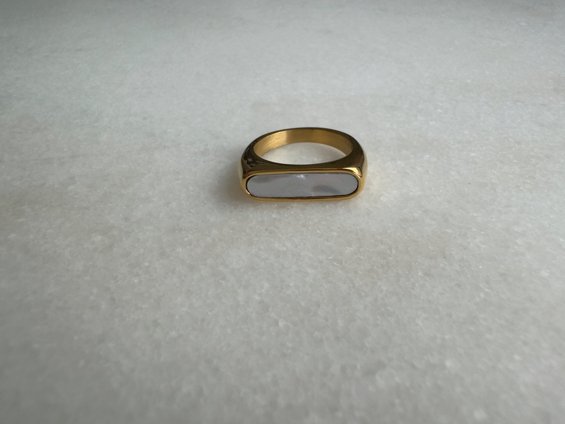Gold signet ring with white enamel on marble background