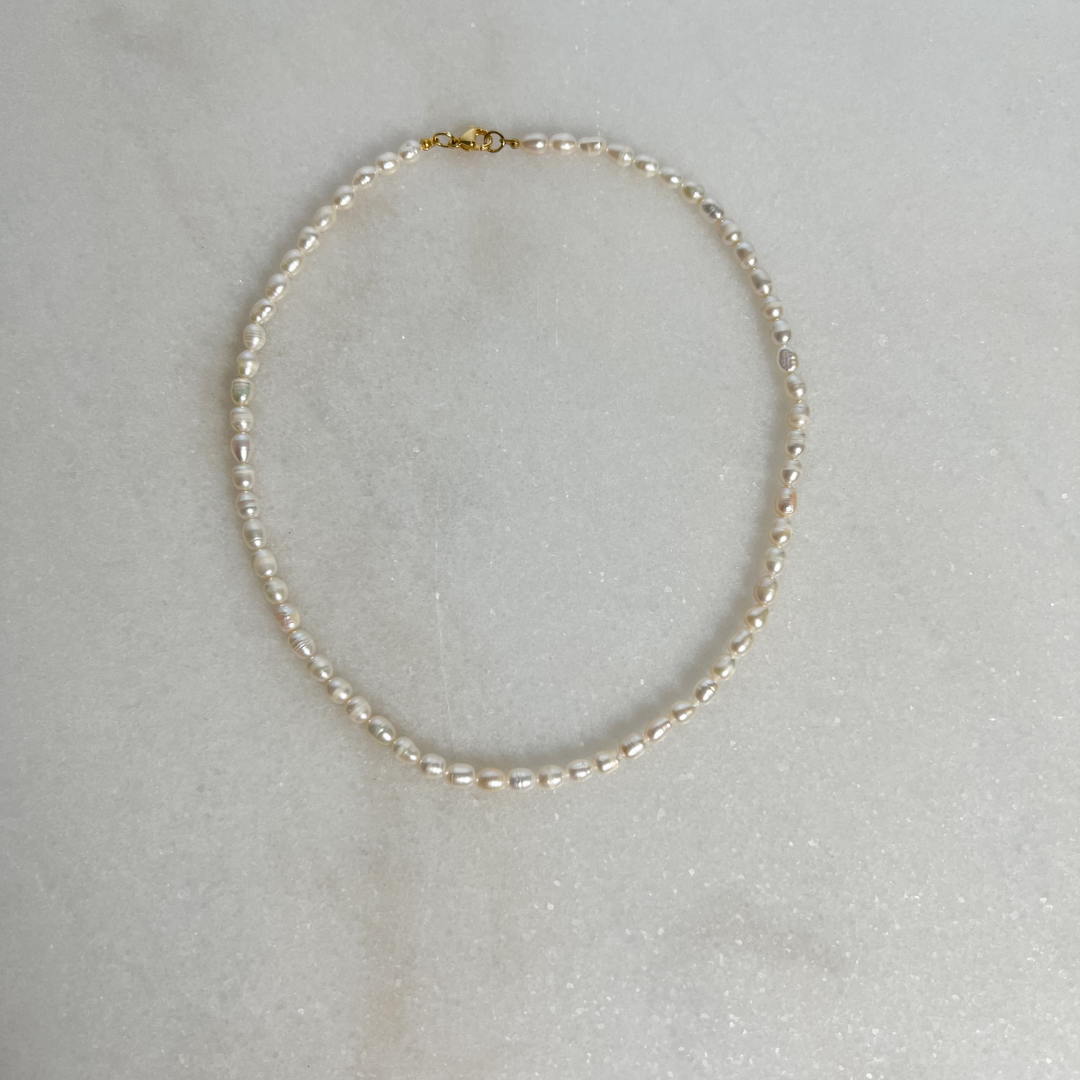 Pearl necklace with gold clasp on marble background.