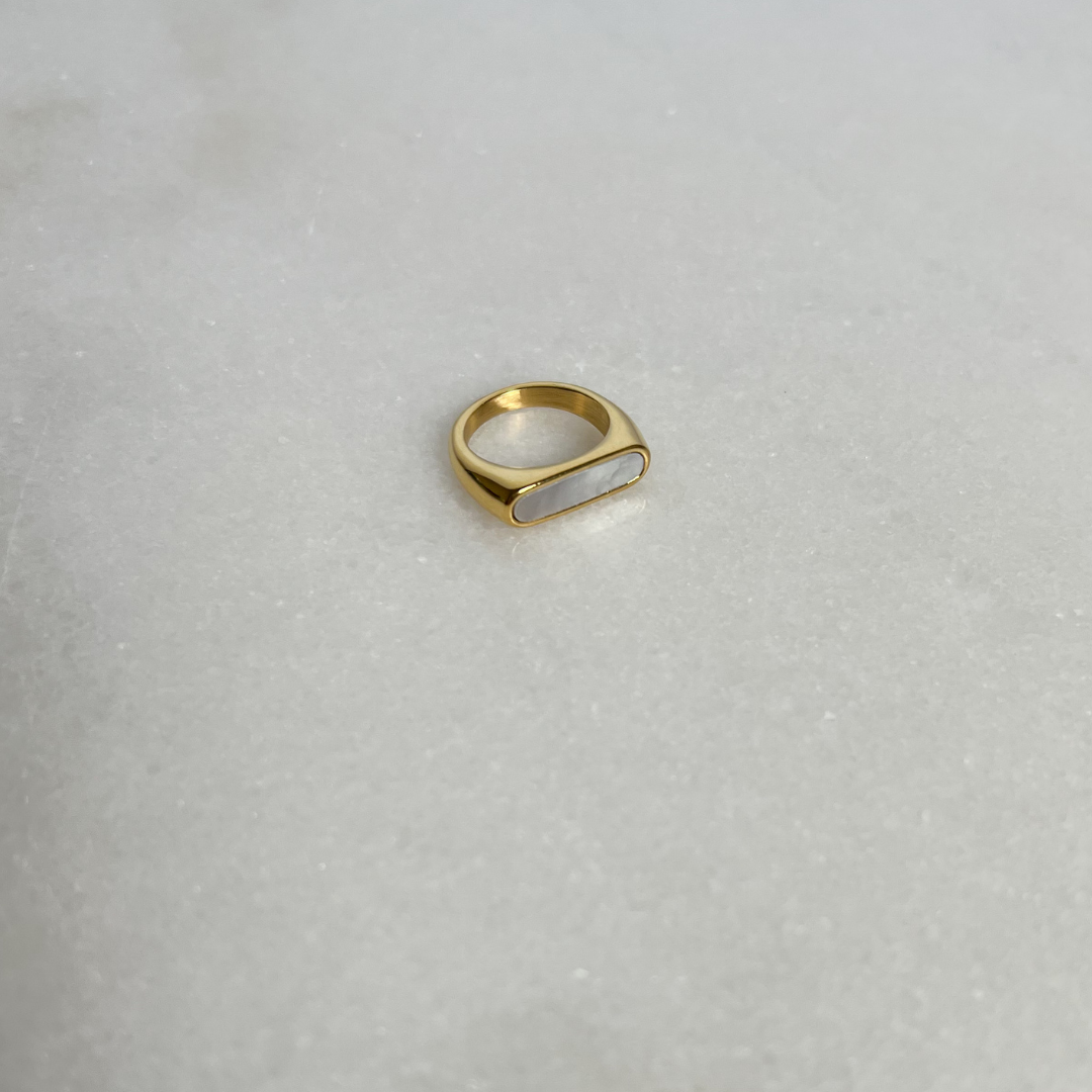 Gold signet ring with white enamel on marble background